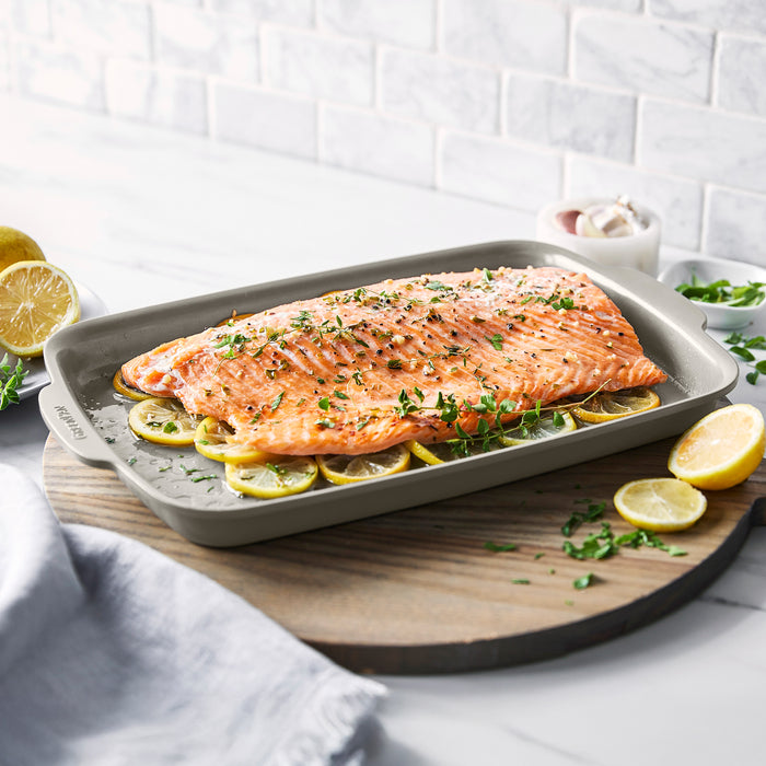 Salmon fillet with herbs on lemon slices in a taupe ceramic nonstick baking pan on a wooden board.