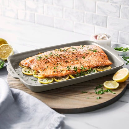 Salmon fillet with herbs on lemon slices in a taupe ceramic nonstick baking pan on a wooden board.