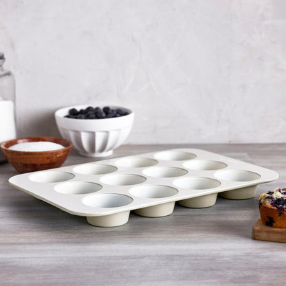 Cream-colored 12-cup muffin pan on a counter, with sugar and blueberries in the background.