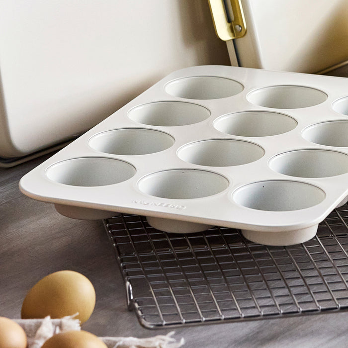 Cream 12-cup muffin pan on cooling rack with several brown eggs, kitchen counter and utensils in the background.