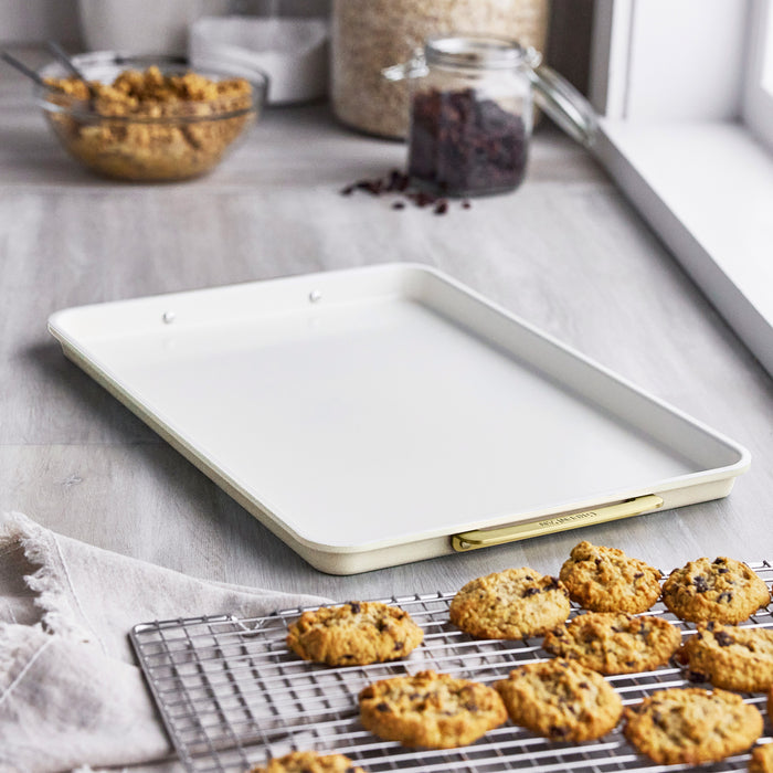 Cream half sheet pan with matching cooling rack on a kitchen counter surrounded by baking ingredients.
