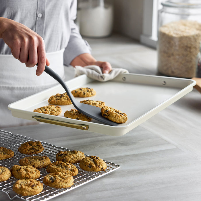 Cookies being lifted from a Reserve Bakeware 13x18 half sheet pan with cooling rack in a kitchen setting.