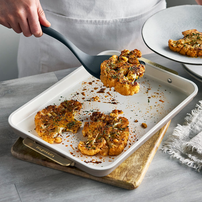 A spatula lifts a seasoned cauliflower steak from a latte-colored Reserve Bakeware 13″ x 9″ quarter sheet pan.