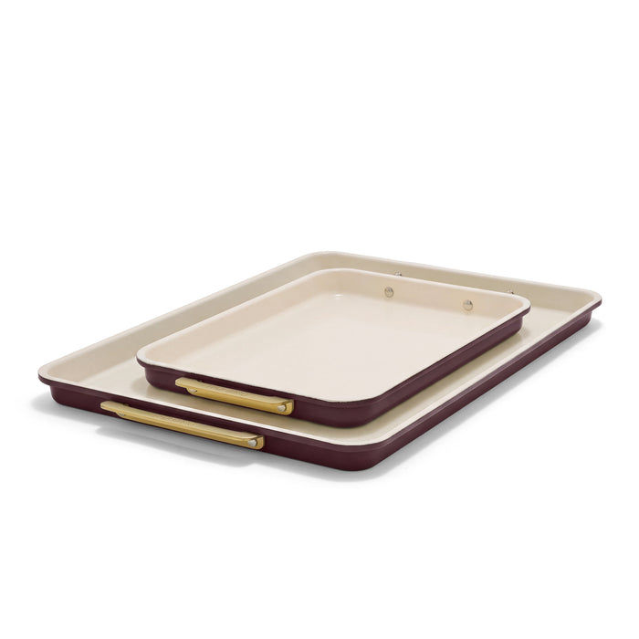 Two rectangular burgundy Reserve Bakeware sheet pans with cream interiors and gold-toned handles.