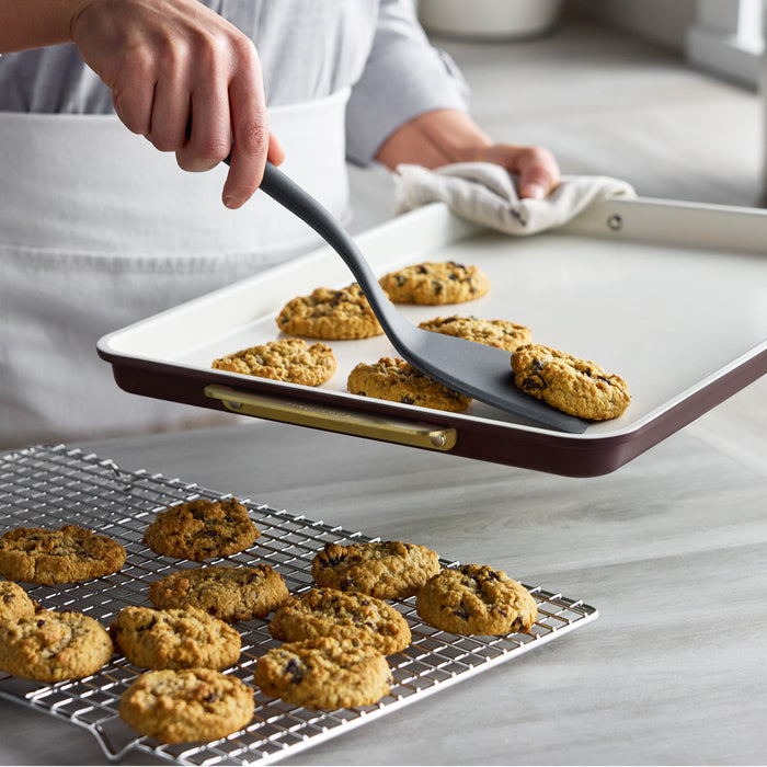A spatula lifting a cookie from a Reserve Bakeware 13″ x 18″ Half Sheet Pan in Bordeaux onto a wire cooling rack.