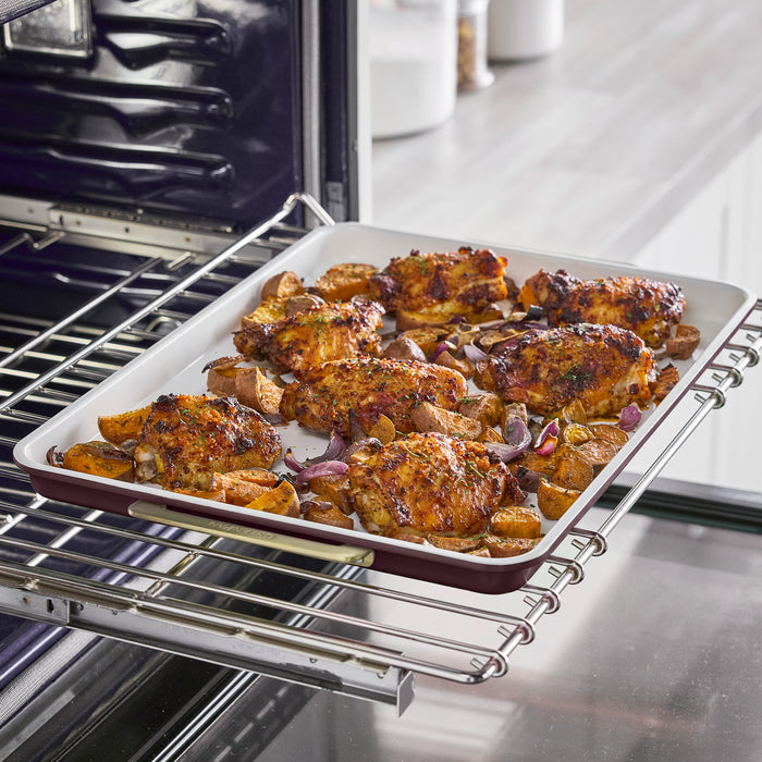 Roasted chicken thighs, potato wedges, and red onions in a Bordeaux 13″ x 18″ Reserve Bakeware half sheet pan inside an oven.