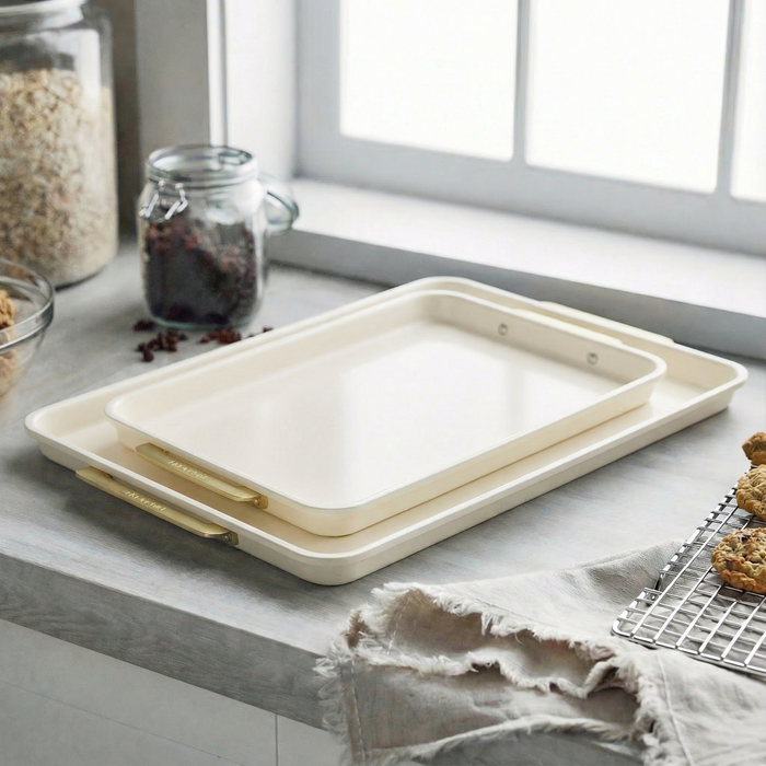 Two cream-colored baking sheets from a 2-piece set are nested together on a kitchen countertop.