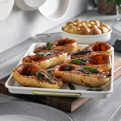 Roasted butternut squash with herbs on a Reserve Bakeware half sheet pan, with a bowl of cream and fresh bread nearby.
