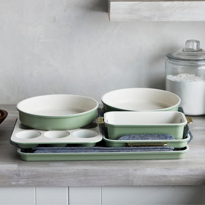 Sage green bakeware set of 8 pieces stacked on a kitchen counter next to a glass jar of flour.