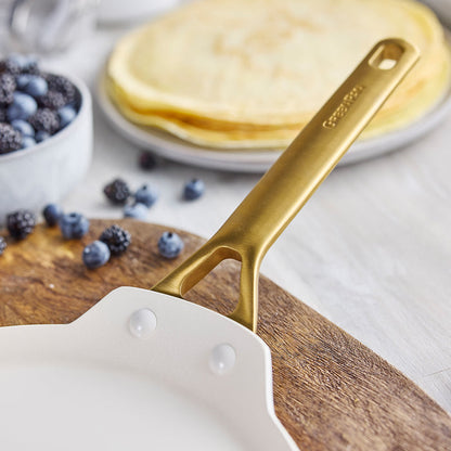 Gold-handled crepe pan with crepes and berries on a wooden board