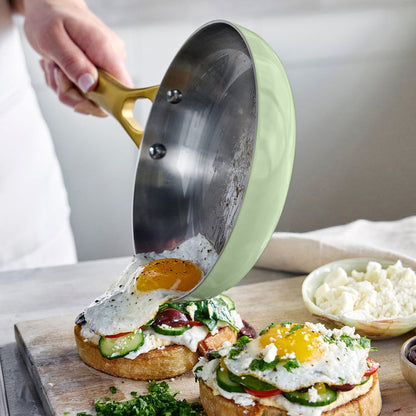 Person using a frypan to place an egg onto a sandwich on a wooden board.