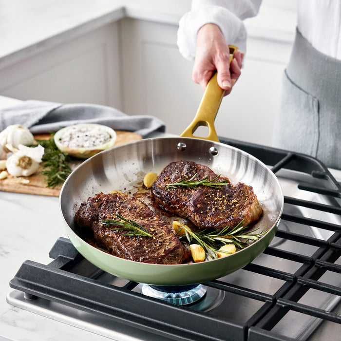 Steaks being cooked in a pan on a stove with a person holding the handle.