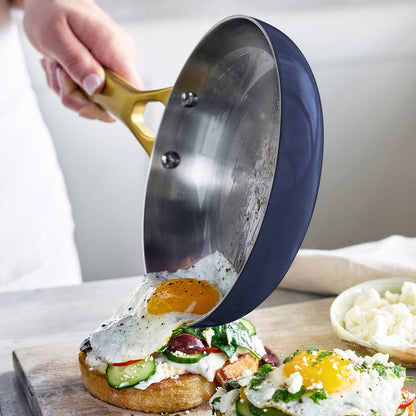 Person using a frypan to place an egg onto a sandwich on a wooden board.