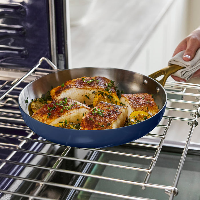 Blue frying pan with cooked fish and vegetables on an oven rack