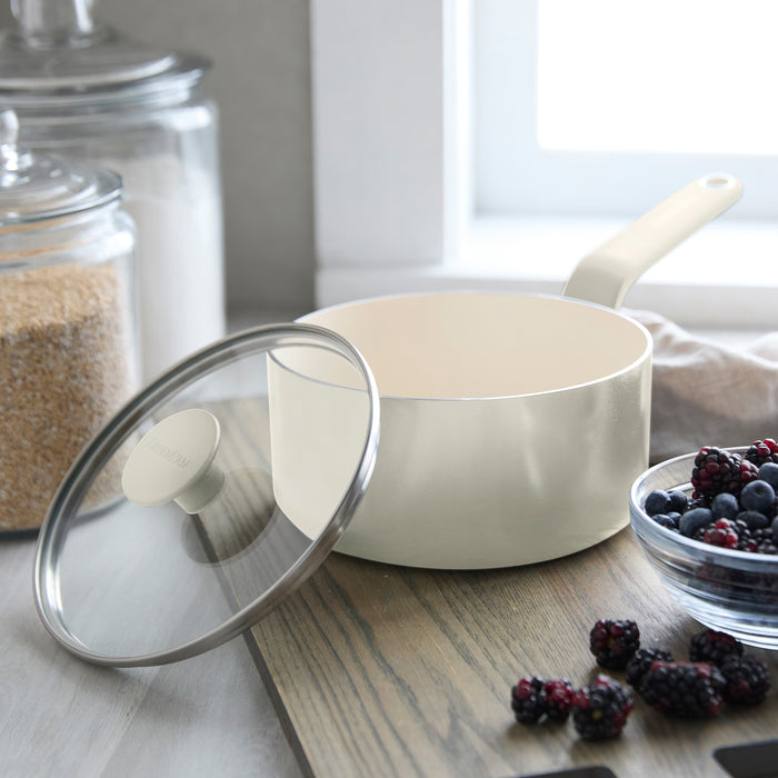 Cream ceramic 2-quart saucepan with lid on wood counter, next to berries and glass jars filled with sugar.