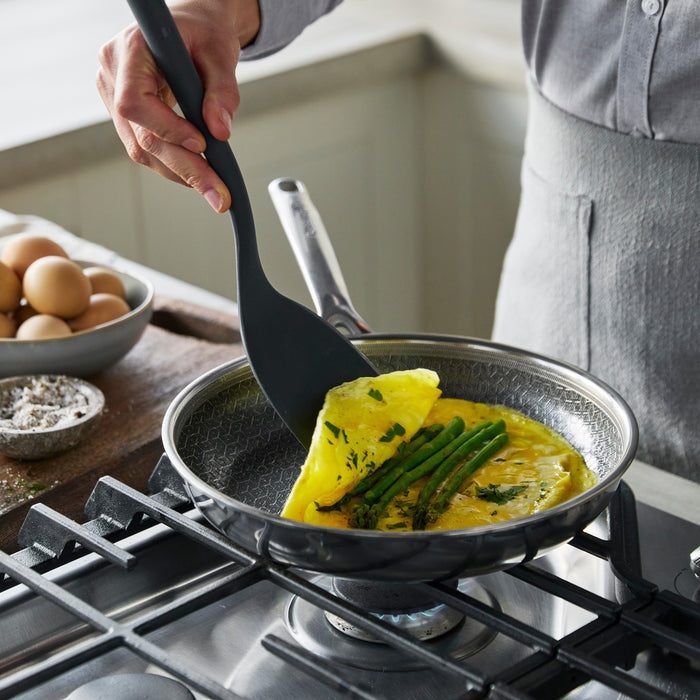 A spatula folding an asparagus omelet in a Spectra Diamond Thermobond hybrid ceramic nonstick frypan on a stovetop.