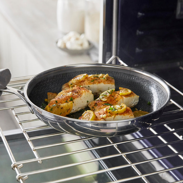 Seared fish fillets and lemon slices in a dark, textured Spectra Diamond Thermobond hybrid ceramic nonstick frypan on an oven rack.