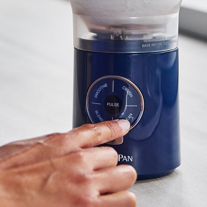 Blue blender with control panel being operated by a hand on a light background