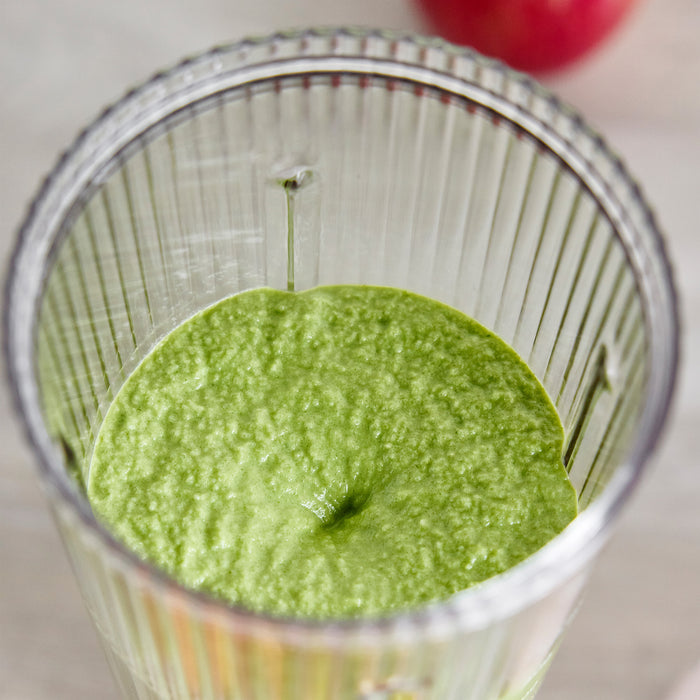 Green smoothie in a clear glass with a blurred background