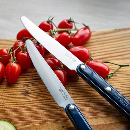 Two knives with blue handles on a wooden cutting board with tomatoes and a zucchini.