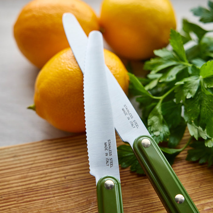 Two knives with green handles on a wooden cutting board with citrus and herbs