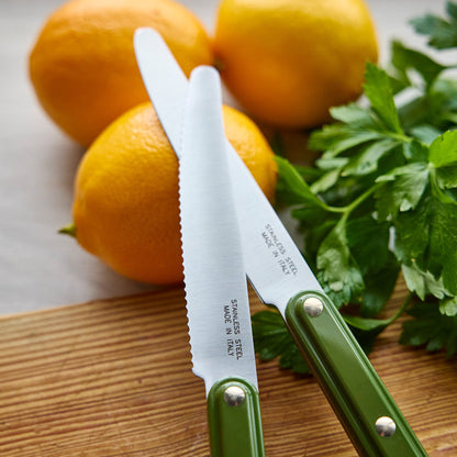 Two knives with green handles on a wooden cutting board with citrus and herbs