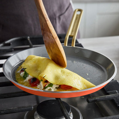 A wooden spatula folds a veggie omelette in a Stanley Tucci 10-inch nonstick crepe and omelette pan on a stovetop.