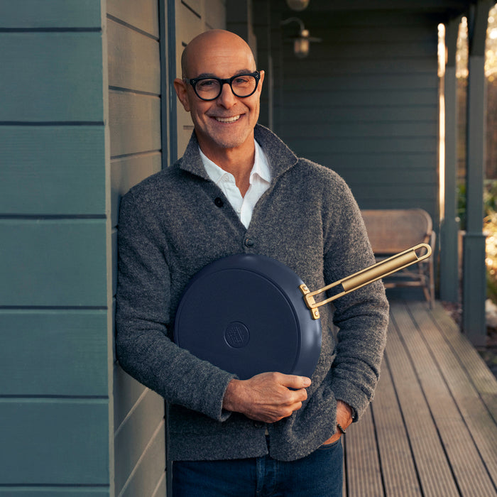 Man in glasses holding a blue ceramic nonstick mini cookware set on a porch with a house in the background.