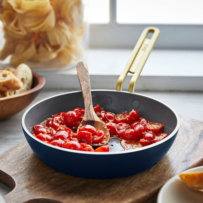 Cherry tomatoes cooking with a wooden spoon in blue ceramic nonstick cookware from a 3-piece mini set.
