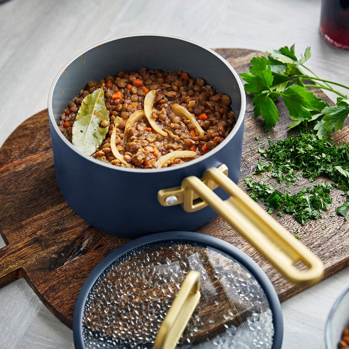 Lentil stew in a white ceramic pot on a wooden board with parsley, part of a 3-piece mini cookware set.
