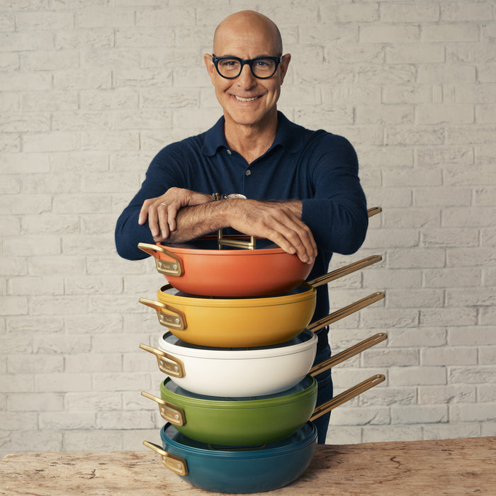 Five Venetian Teal Stanley Tucci 4.5-quart pans arranged on a table with a smiling man standing behind them.