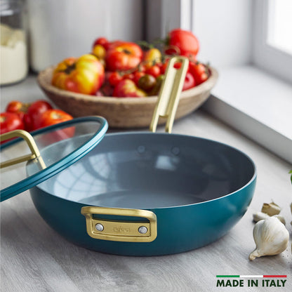 Venetian teal ceramic nonstick pan with glass lid, next to tomatoes and garlic on a surface.