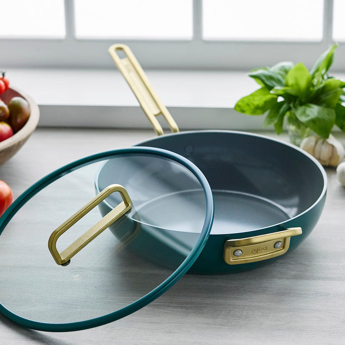 Teal ceramic 4.5-quart pan with gold handle on a counter, fresh basil nearby.