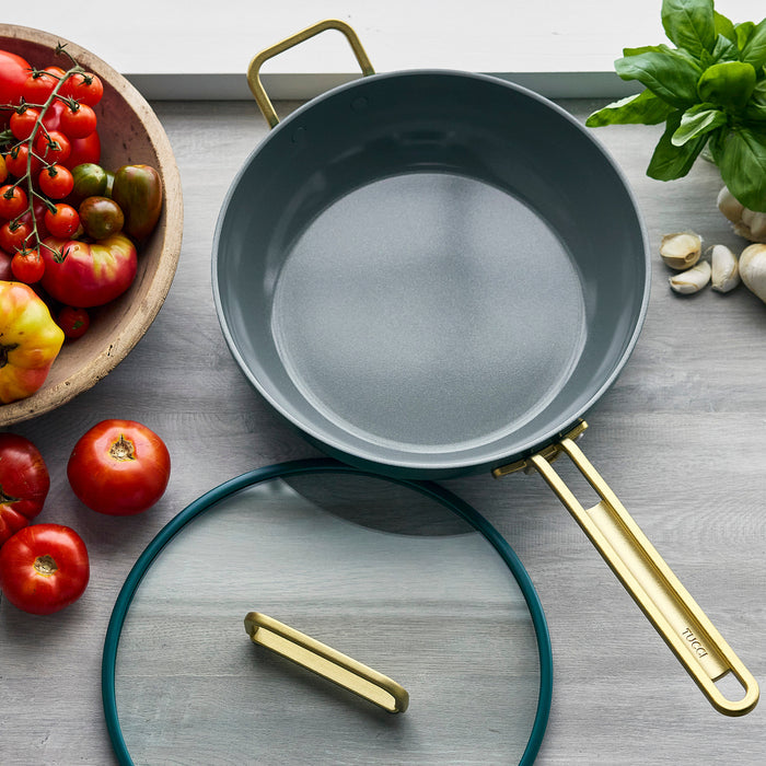 Venetian teal ceramic 4.5-quart pan with gold handle and glass lid on a gray countertop.