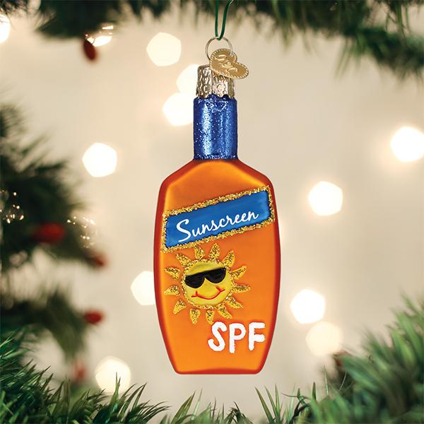 An ornament shaped like an orange sunscreen bottle with a sun wearing sunglasses and â€œSPFâ€_x009d_ written on it, hanging on a Christmas tree with blurred lights in the background.