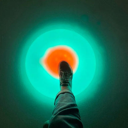 Foot stepping onto the TFH Illuminated Floor Splot, glowing teal with an orange centre, an interactive floor light for sensory play and movement