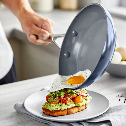 Person sliding a fried egg from a frypan onto avocado toast