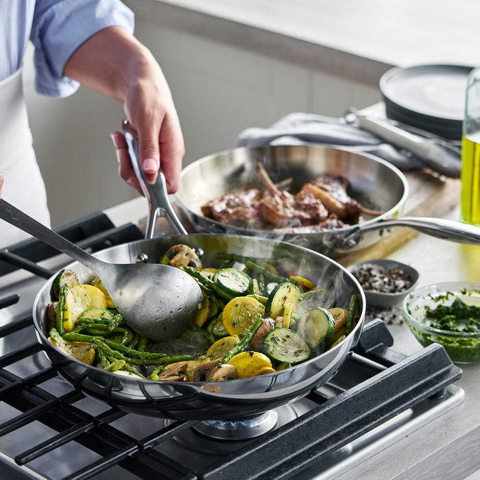 Zucchini, mushrooms, and green beans being sautéed in a stainless steel frypan with steak resting nearby.