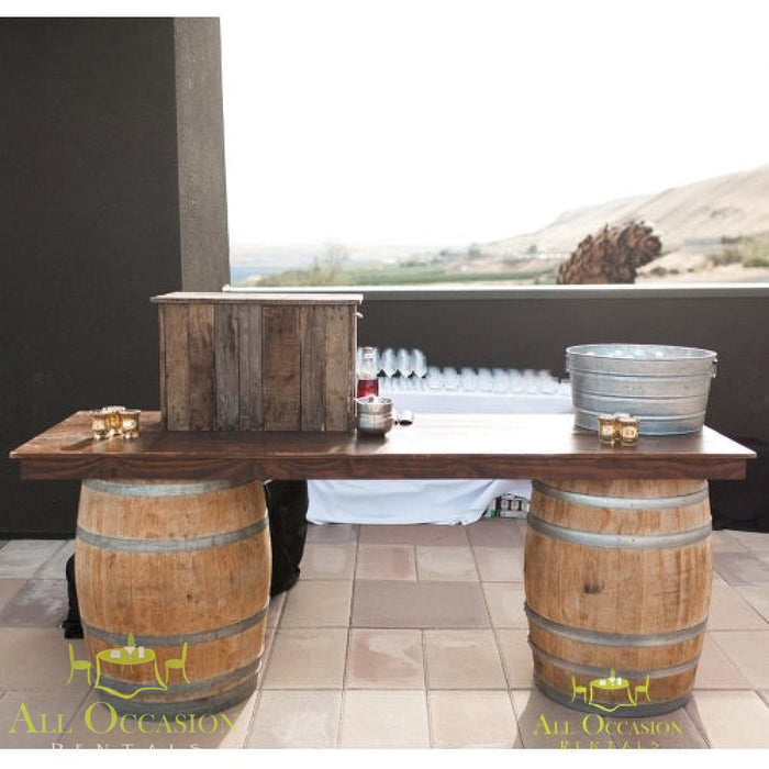 Wine barrel bar or table, 72" L x 30" W, featuring rustic wooden top and barrel legs at an outdoor venue.